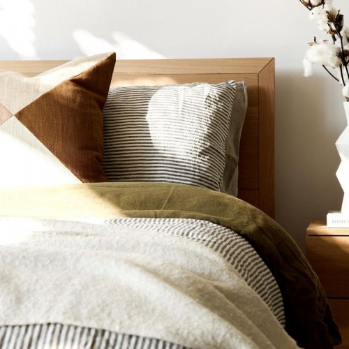 Sleep in style swath of sunlight shines across a well made bed and bedside table with a vase of cotton plants